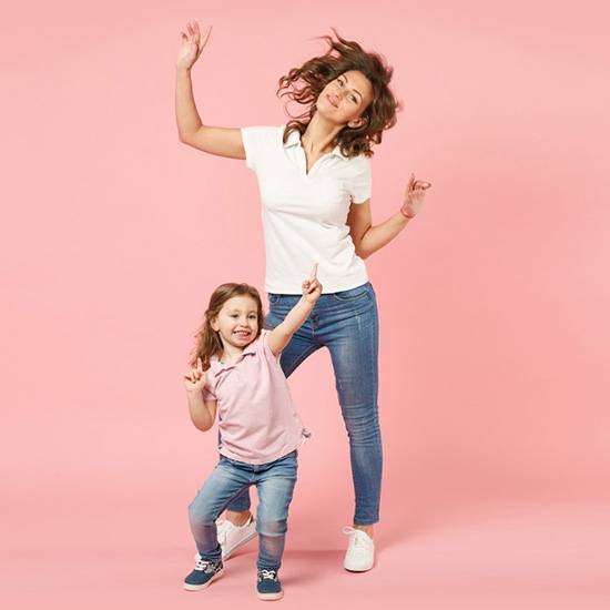 Mother and young daughter dancing in front of pink background