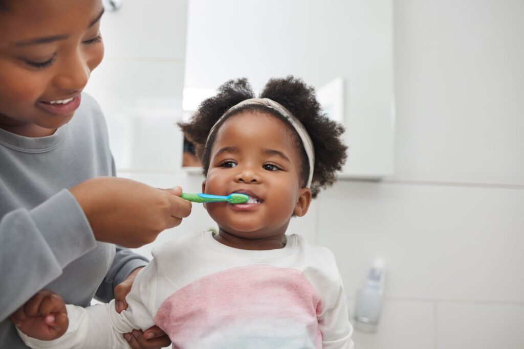 A little girl helping brush her little sister's teeth.